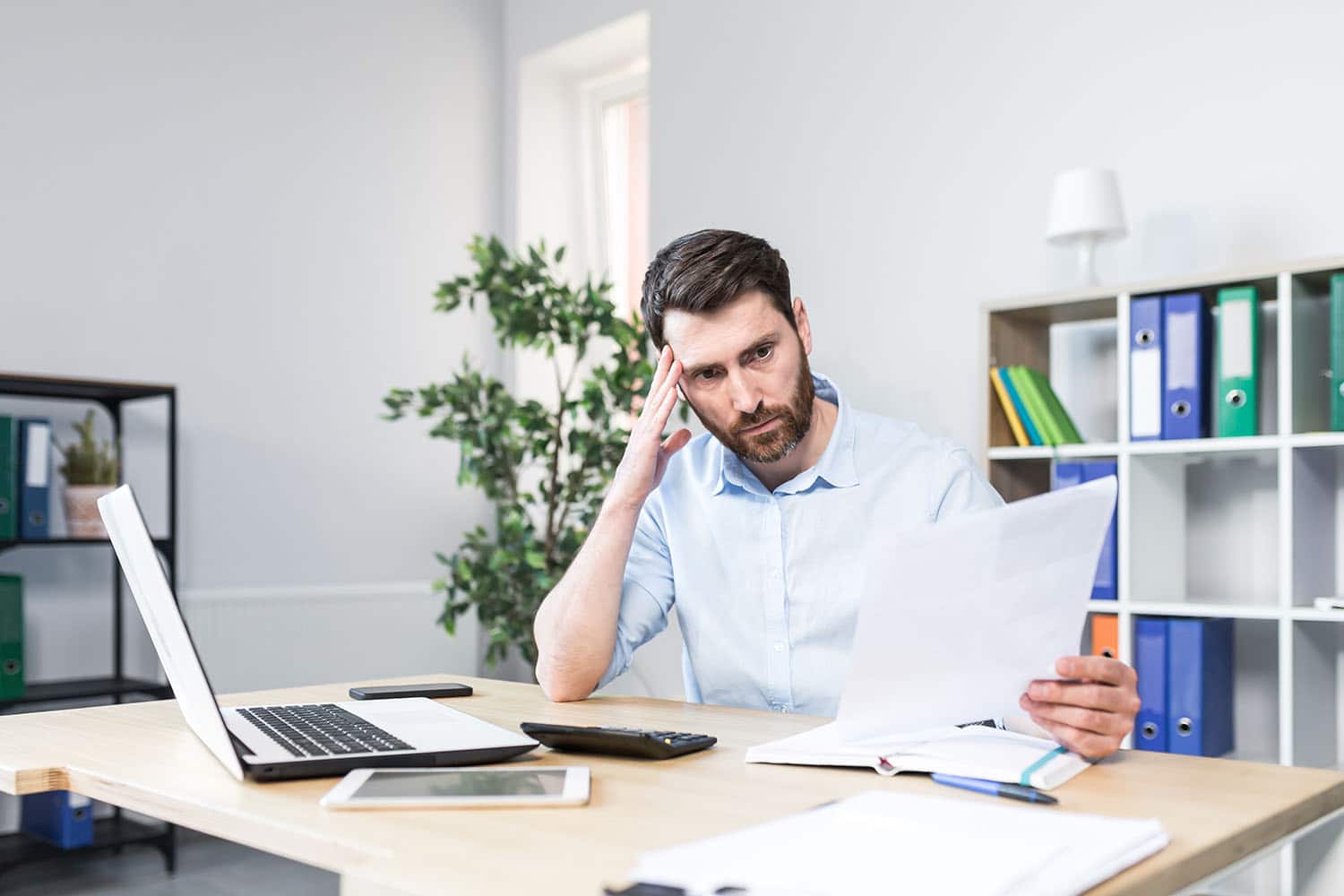 Man looks frustrated with a piece of paper in his hand, he is suffering from a late payment and is considering payment solutions for small businesses.